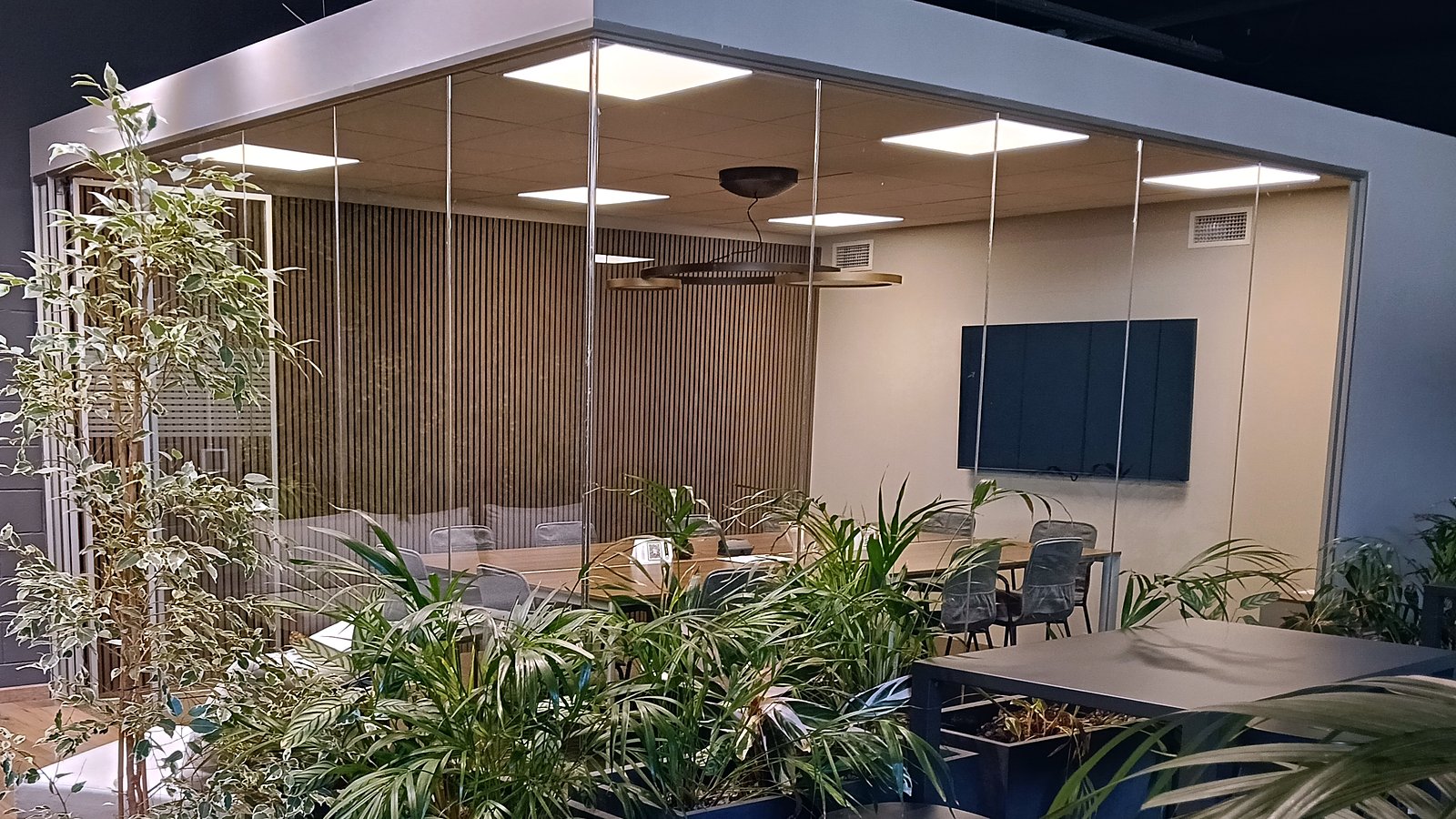 Sala riunioni vetrata vista dall'area relax con parete verde – Media Solution